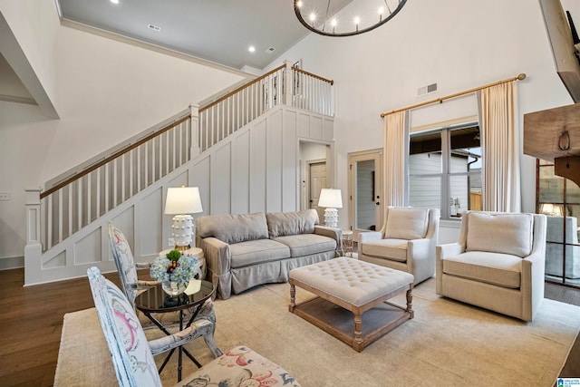 living room with a towering ceiling, an inviting chandelier, and light wood-type flooring