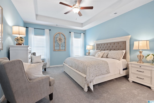 bedroom with ceiling fan, light colored carpet, and a tray ceiling