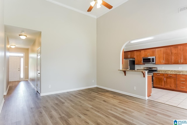 kitchen featuring appliances with stainless steel finishes, light stone counters, light tile patterned floors, ceiling fan, and a breakfast bar