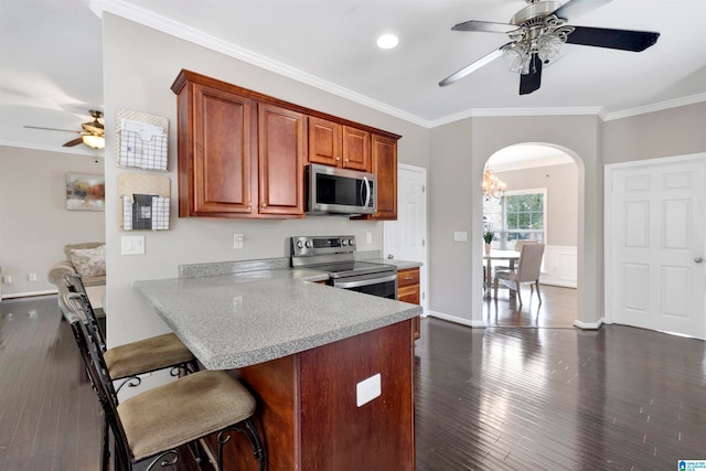 kitchen featuring dark wood finished floors, crown molding, light countertops, appliances with stainless steel finishes, and a kitchen breakfast bar