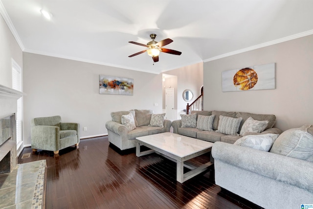 living area featuring dark wood-style flooring, crown molding, a fireplace, stairway, and a ceiling fan