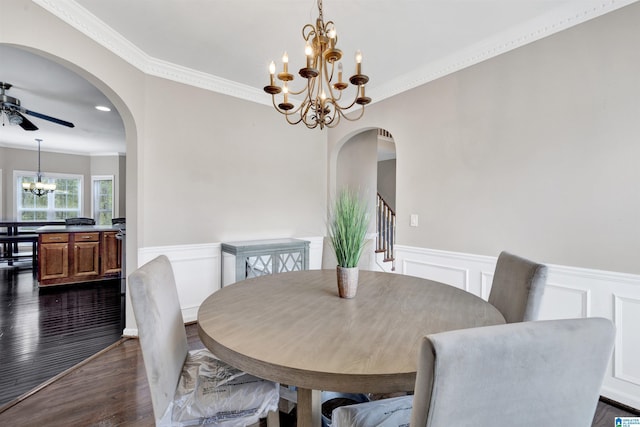 dining room featuring arched walkways, ceiling fan with notable chandelier, wainscoting, dark wood-style floors, and crown molding