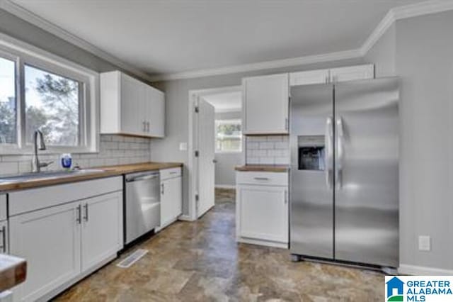 kitchen with crown molding, tasteful backsplash, appliances with stainless steel finishes, white cabinets, and a sink