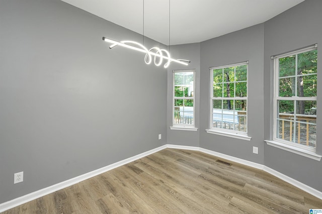 empty room featuring an inviting chandelier, baseboards, visible vents, and wood finished floors