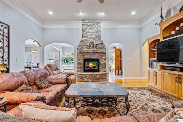 living area with arched walkways, a fireplace, crown molding, and light wood finished floors