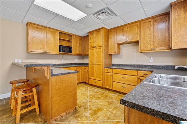 kitchen with black microwave, a breakfast bar, a sink, visible vents, and open shelves