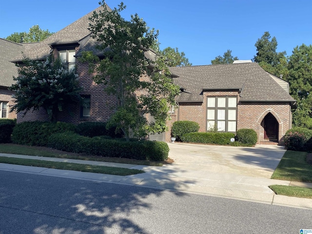 view of front of property featuring driveway, brick siding, and roof with shingles