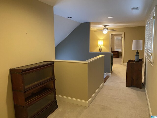 hallway featuring baseboards, visible vents, light colored carpet, and an upstairs landing