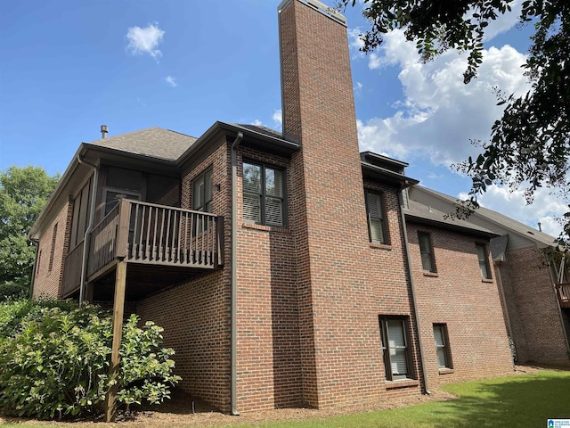 back of house with brick siding, a chimney, and a balcony