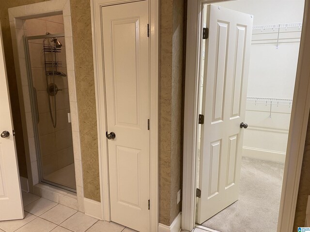 full bathroom featuring a shower stall, a walk in closet, and tile patterned floors