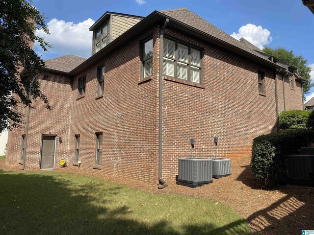 view of side of home with brick siding, a yard, and central AC