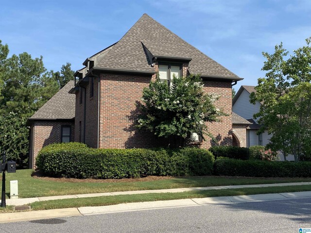 view of side of property with a shingled roof, brick siding, and a lawn