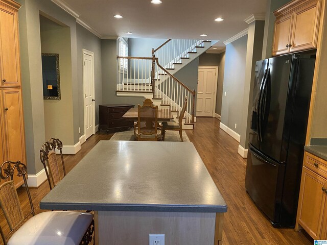 kitchen with dark wood-style flooring, crown molding, recessed lighting, black fridge with ice dispenser, and a kitchen island