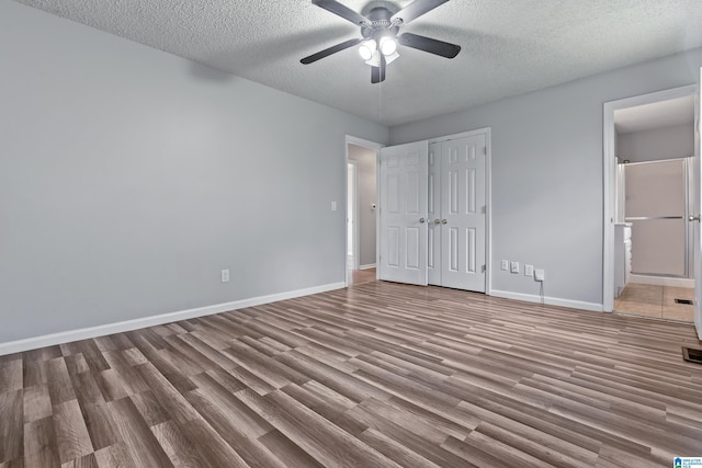 unfurnished bedroom with a textured ceiling, light wood-type flooring, ensuite bath, and baseboards