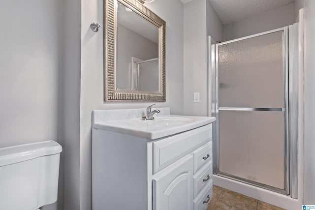 bathroom featuring toilet, a shower stall, vanity, a textured ceiling, and tile patterned flooring