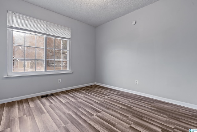 spare room featuring visible vents, a textured ceiling, baseboards, and wood finished floors