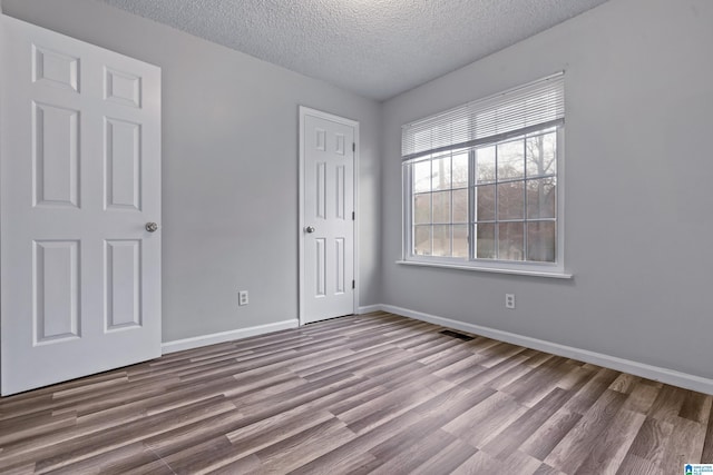 unfurnished room with baseboards, a textured ceiling, visible vents, and light wood-style floors