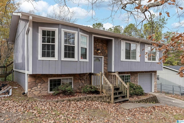 bi-level home featuring stone siding, an attached garage, concrete driveway, and fence