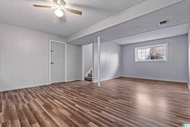 empty room featuring a textured ceiling, dark hardwood / wood-style flooring, ceiling fan, and wooden walls