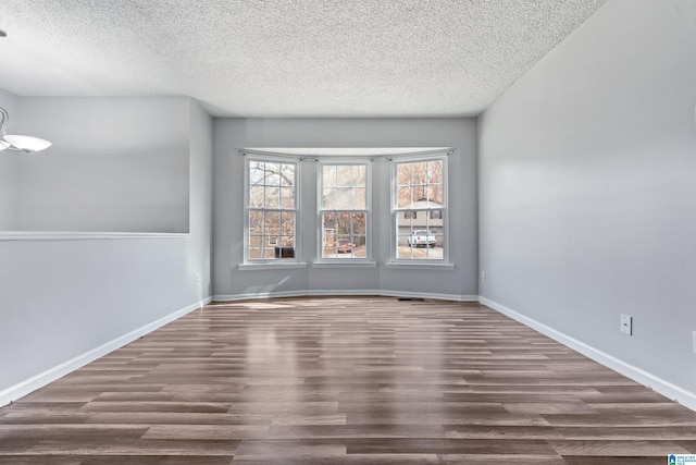 empty room featuring a textured ceiling, dark wood-style flooring, and baseboards