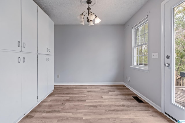 unfurnished dining area featuring visible vents, an inviting chandelier, light wood-style floors, a textured ceiling, and baseboards