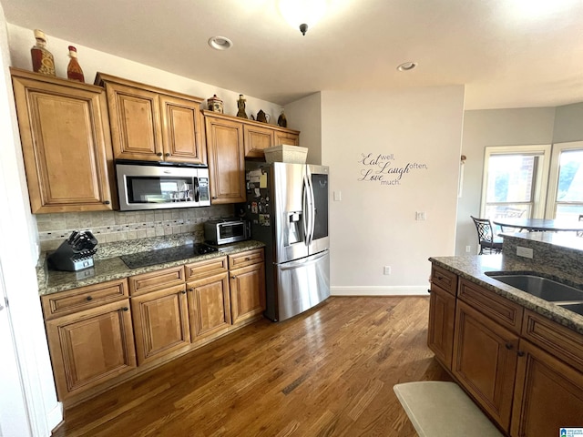 kitchen with stone counters, stainless steel appliances, decorative backsplash, brown cabinetry, and dark wood finished floors