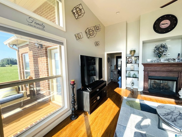 living room featuring a towering ceiling, baseboards, wood finished floors, and a glass covered fireplace