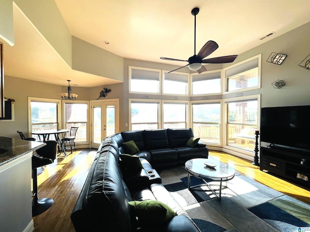 living area with light wood finished floors, a high ceiling, visible vents, and ceiling fan with notable chandelier