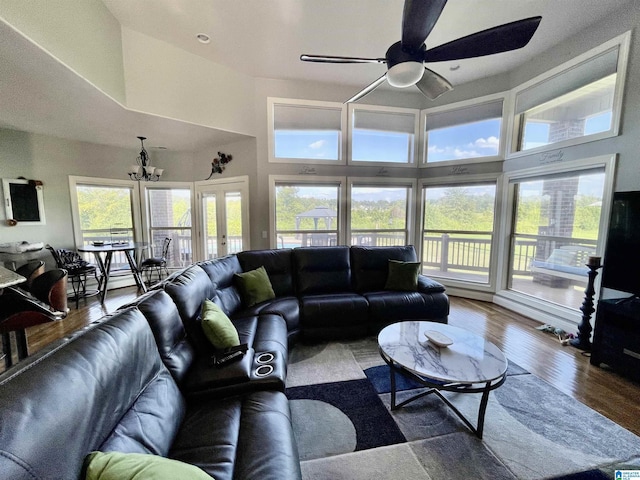 living room with a towering ceiling, plenty of natural light, wood finished floors, and ceiling fan with notable chandelier