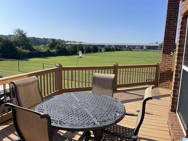 wooden terrace featuring fence, outdoor dining area, and a lawn