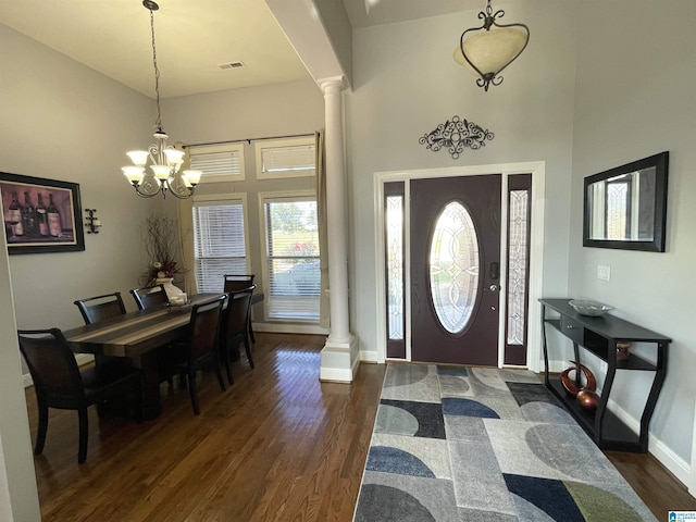 entryway with a towering ceiling, decorative columns, dark wood-type flooring, and a chandelier