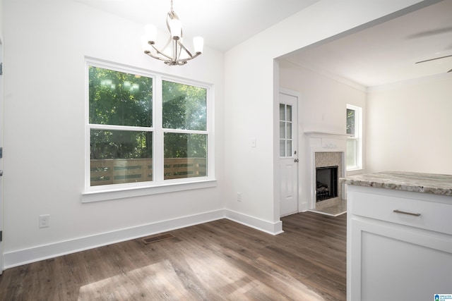 unfurnished dining area featuring visible vents, baseboards, a fireplace with flush hearth, wood finished floors, and a notable chandelier