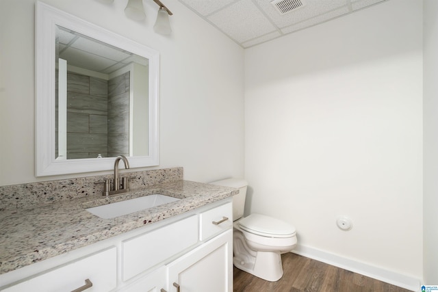 bathroom with a drop ceiling, toilet, vanity, and wood-type flooring