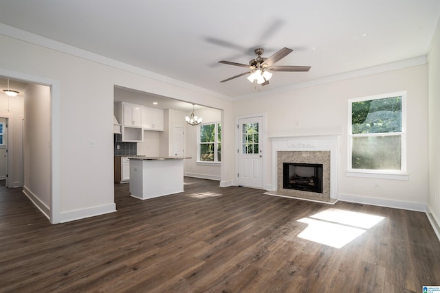 unfurnished living room featuring ornamental molding, dark wood-type flooring, plenty of natural light, and ceiling fan with notable chandelier