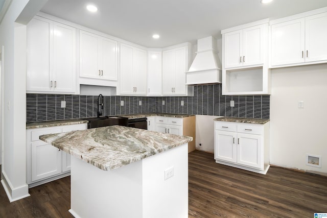 kitchen featuring premium range hood, dark hardwood / wood-style floors, tasteful backsplash, white cabinets, and a center island