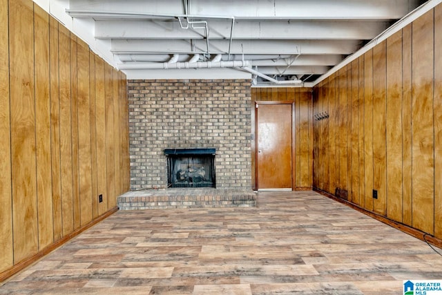 basement featuring wood walls, wood-type flooring, brick wall, and a brick fireplace