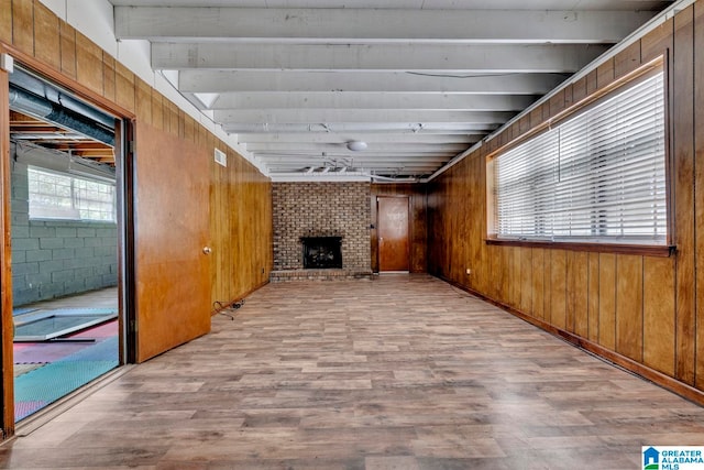 interior space with brick wall, beamed ceiling, light wood-type flooring, and a brick fireplace