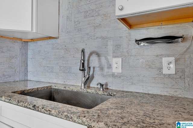 kitchen with white cabinetry, sink, and light stone countertops