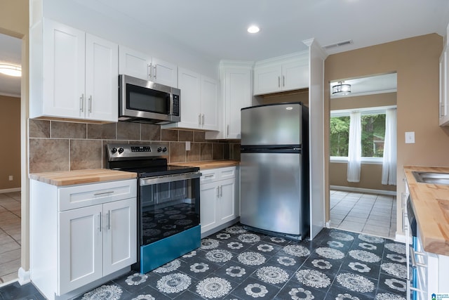 kitchen featuring backsplash, white cabinets, butcher block counters, dark tile patterned flooring, and stainless steel appliances