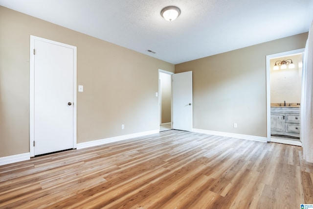 unfurnished bedroom with light hardwood / wood-style floors and connected bathroom