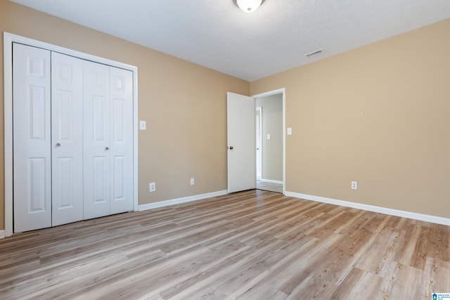 unfurnished bedroom with a textured ceiling, a closet, and light hardwood / wood-style floors