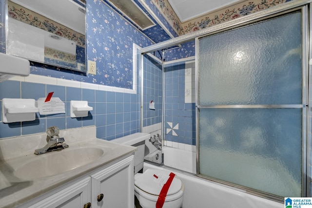 bathroom with a wainscoted wall, tile walls, bath / shower combo with glass door, toilet, and wallpapered walls