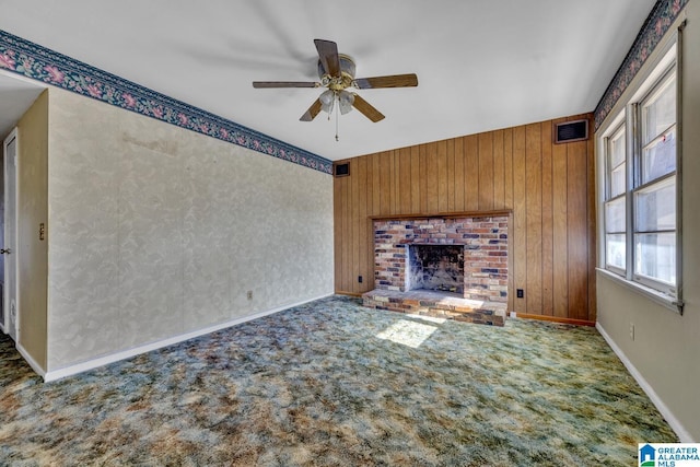 unfurnished living room with carpet floors, wooden walls, a fireplace, and a ceiling fan