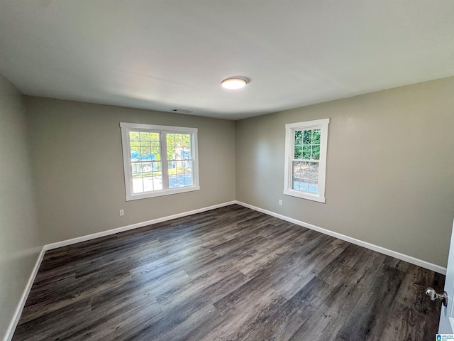 unfurnished room with plenty of natural light, baseboards, visible vents, and dark wood-type flooring