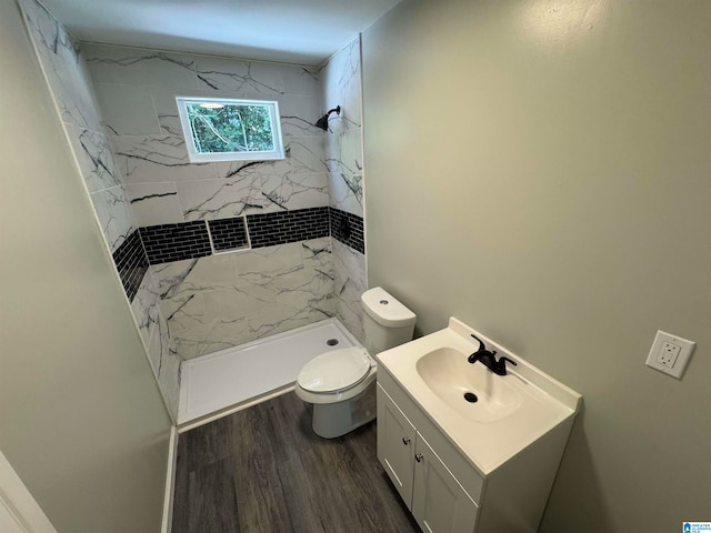 bathroom featuring wood-type flooring, toilet, a tile shower, and vanity