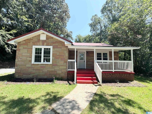 view of front of home featuring a front lawn, metal roof, covered porch, and stone siding