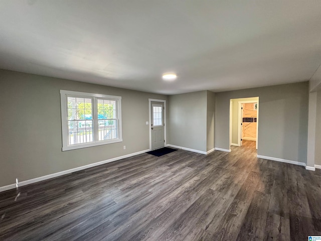 unfurnished living room featuring baseboards and dark wood-style flooring