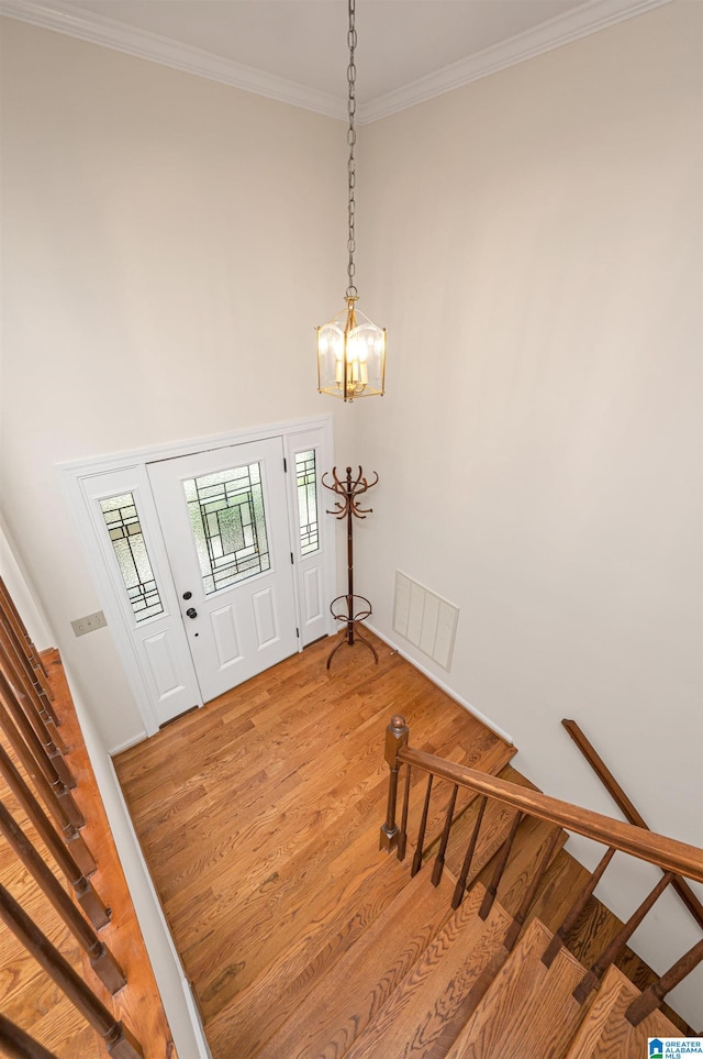 entryway featuring crown molding, a towering ceiling, hardwood / wood-style floors, and a notable chandelier