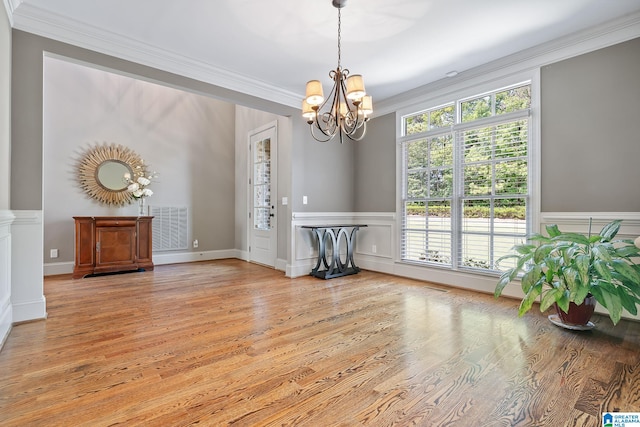 unfurnished dining area with a chandelier, light wood-style flooring, a decorative wall, visible vents, and ornamental molding