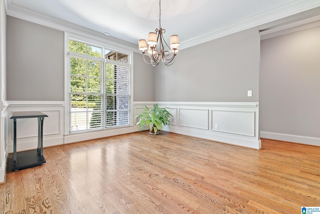 empty room featuring a chandelier, a wainscoted wall, wood finished floors, and crown molding